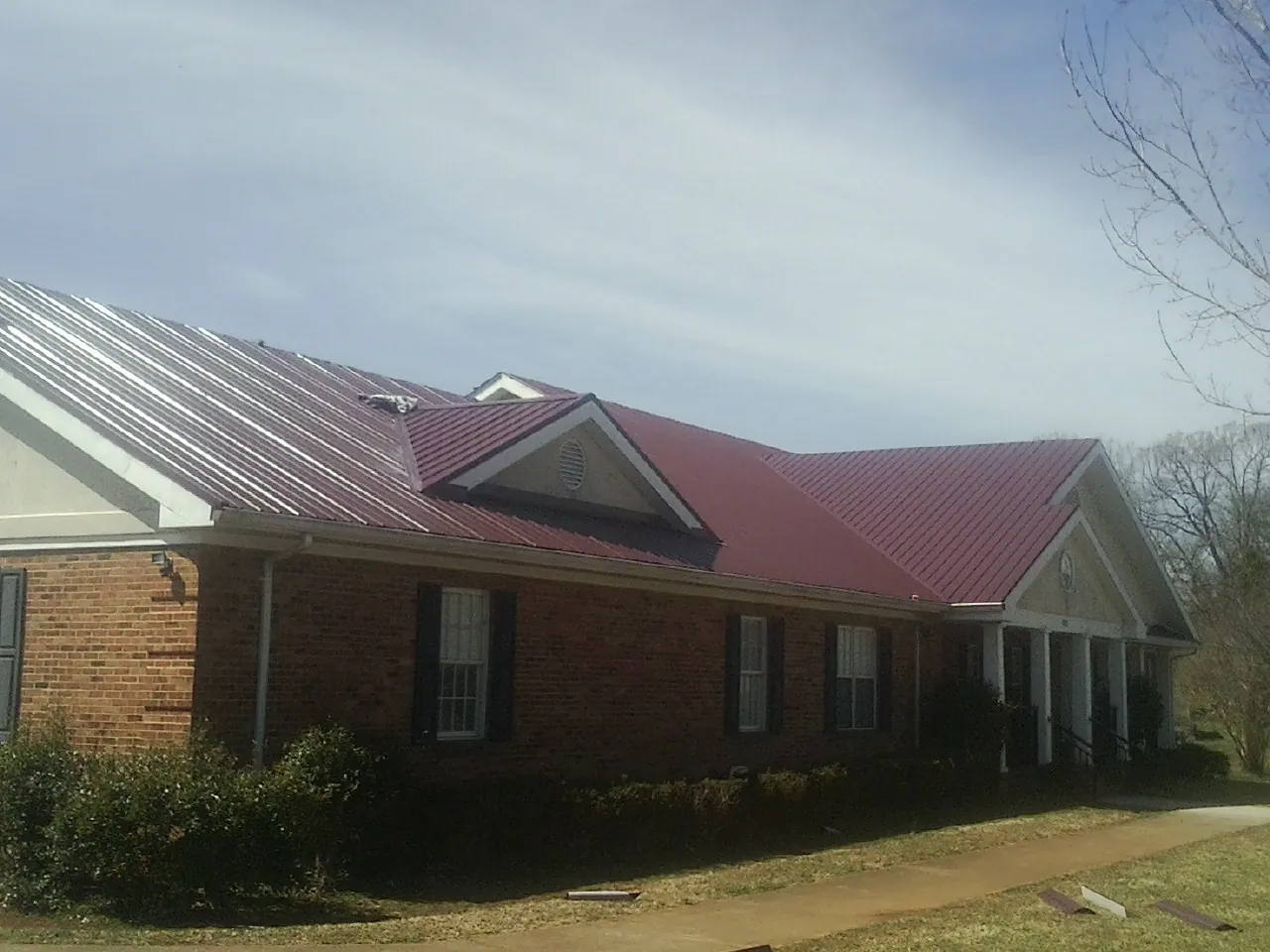Red metal roof with gabled entries on a long brick building, from a Hail Damage Roof Repair job in Fishers