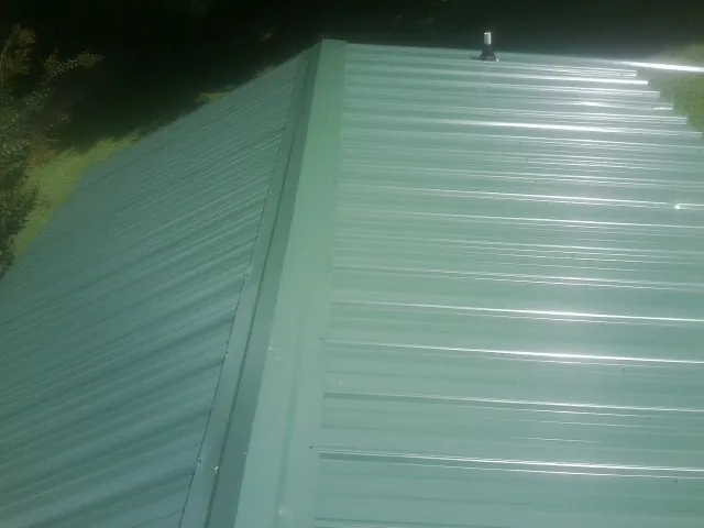 New green metal panels meeting at the ridge of a roof — Flat Roof Repair work by our crew in Fishers